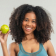 A woman in athletic clothing smiles and holds up a green apple against a plain background.