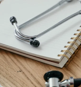 A stethoscope rests on an open spiral notebook placed on a wooden surface.